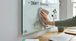 A detailed demonstration illustration of a hand effortlessly wiping dry-erase marker from the stain-free, non-porous glass whiteboard surface.