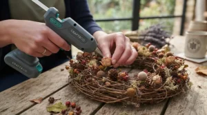 Using a hot glue gun for crafts to attach foliage to a handmade autumn door wreath.