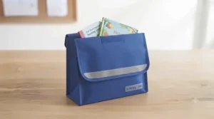 Traditional British school book bag with a safety reflective strip and a reading diary peeking out.